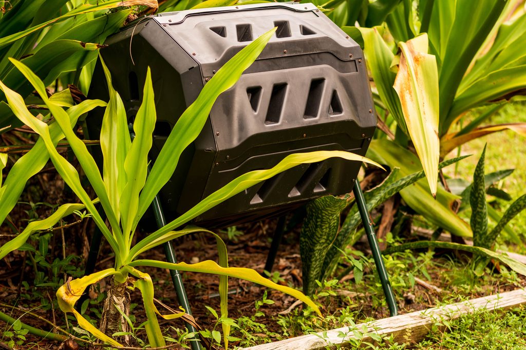A black plastic compost tumbler in a garden
