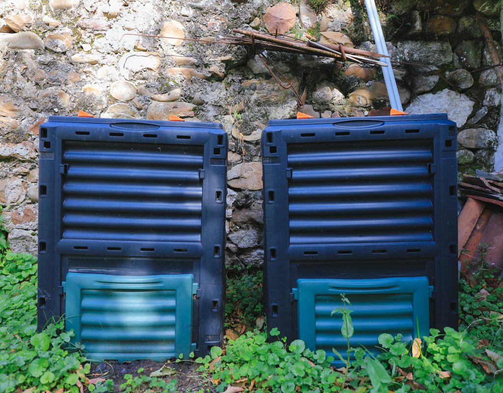 Two rectangular compost bins against a stone wall, set slightly into the ground