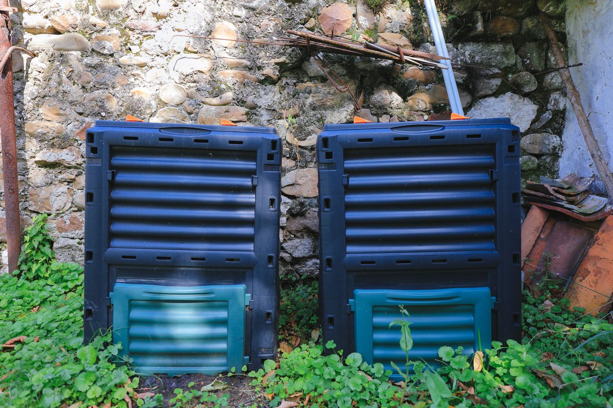 Two rectangular compost bins against a stone wall, set slightly into the ground