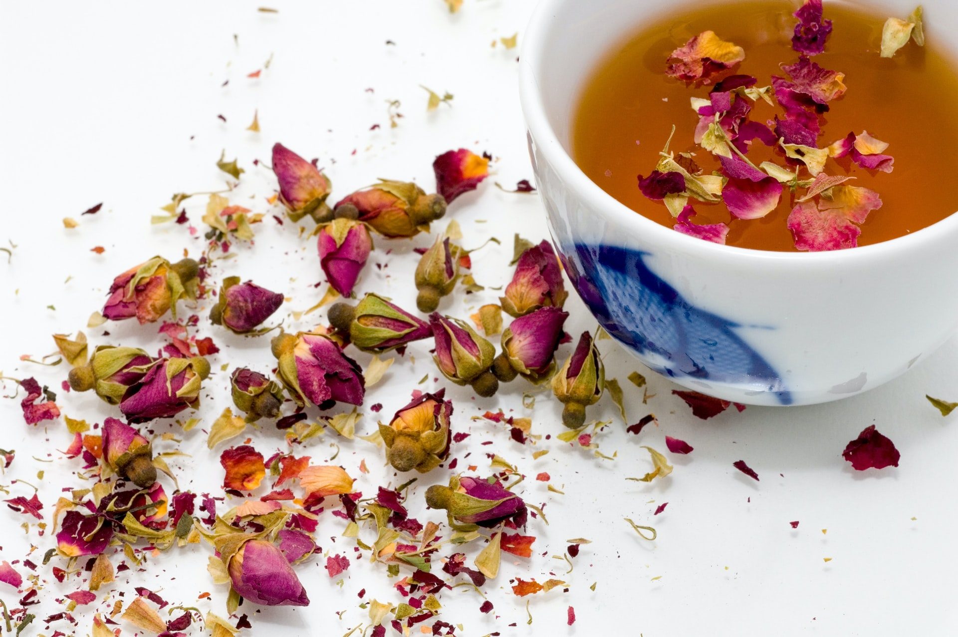 Dried rose petals in a blue and white tea cup with tea, and dried rose buds on the table next to the cup