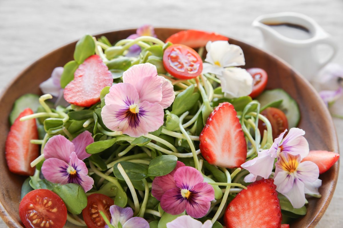 Brown bowl holding pansies, cherry tomatoes, strawberries, and sunflower sprouts