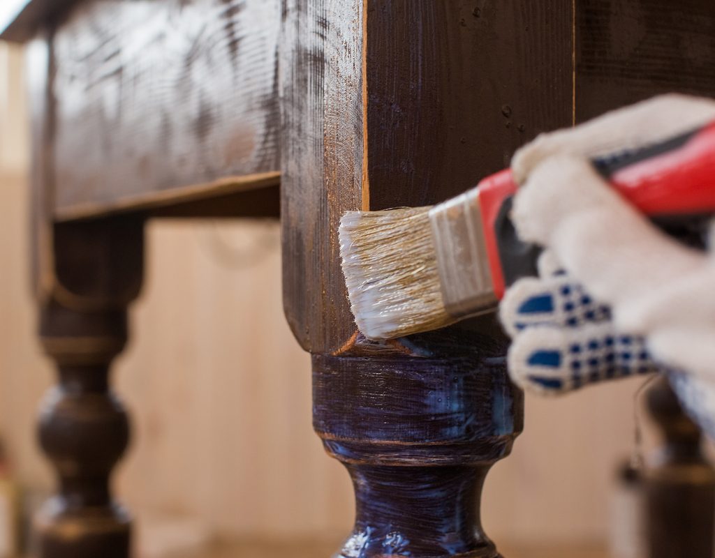 Gloved hand painting a wooden chair leg