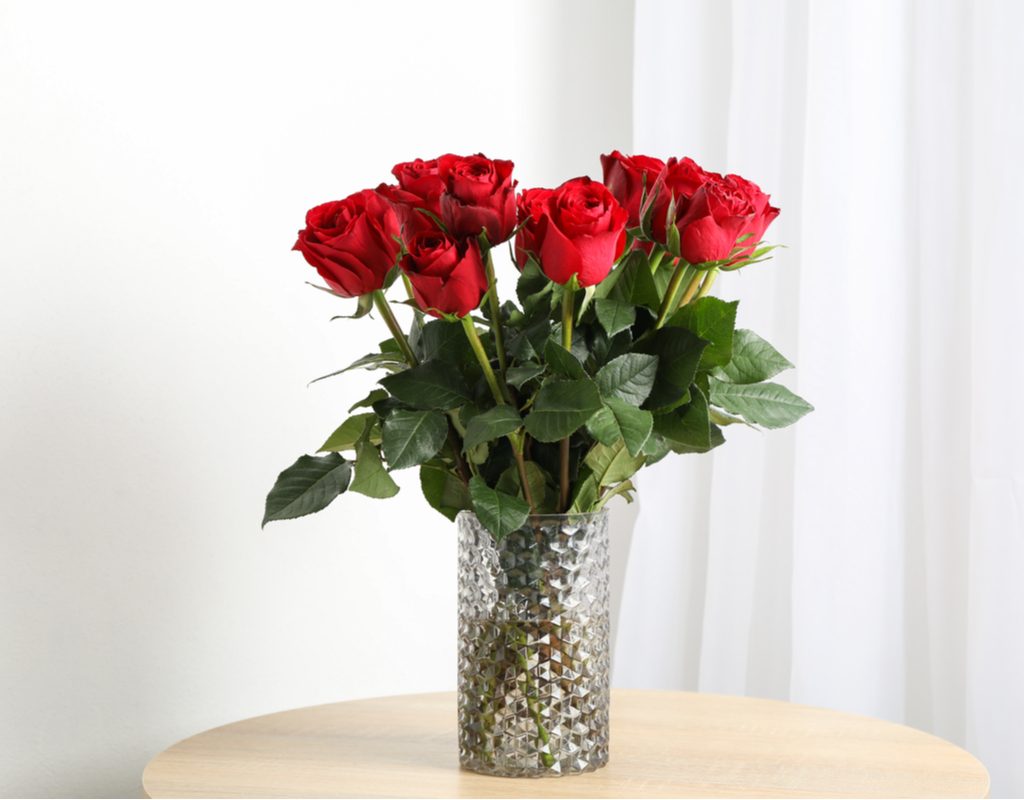 Red roses in a clear vase, on a light brown table against a white background