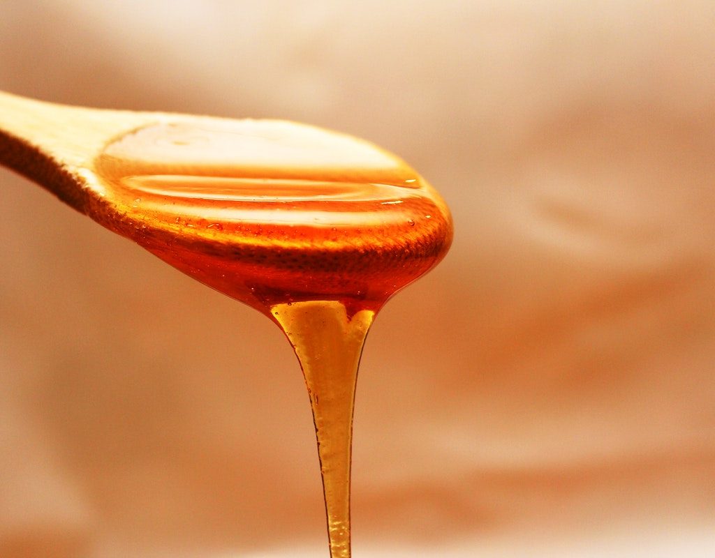 A wooden spoon full of honey, which is dripping off of it.
