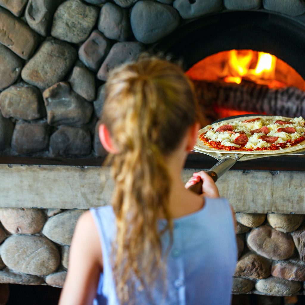 Little Girl Putting Pizza Into Oven