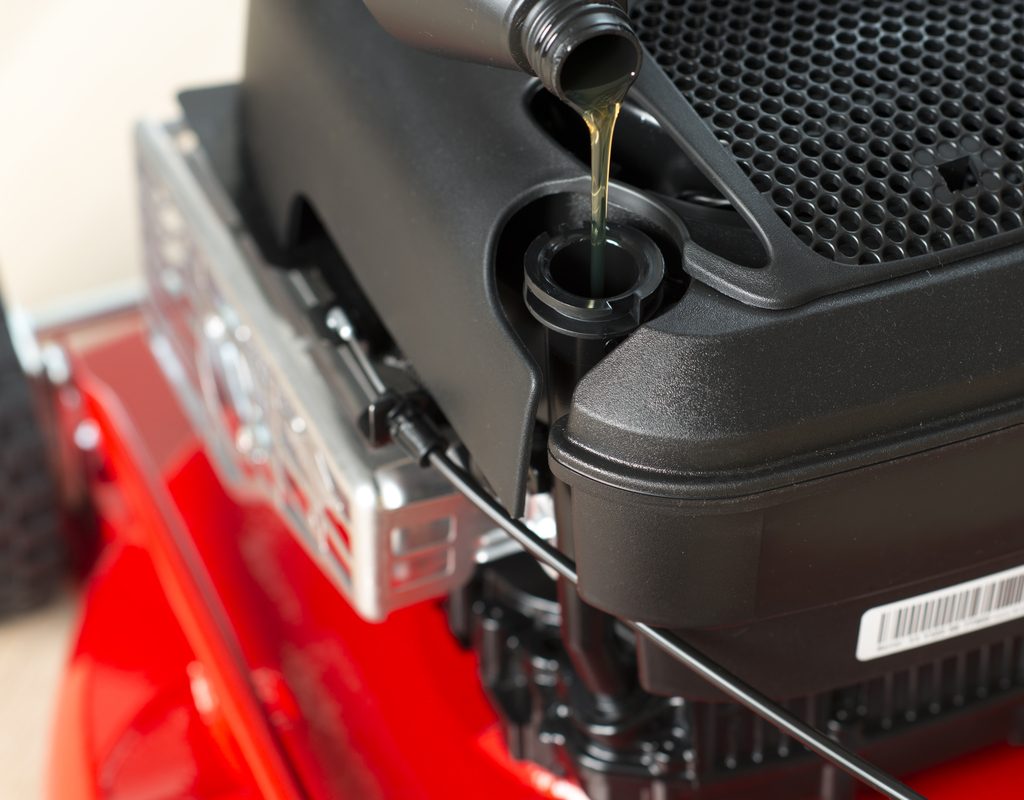 Oil slowly pouring into the engine of a lawn mower