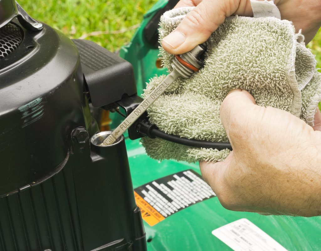 Person removing oil dipstick from lawn mower and wiping it with old, white wash rag