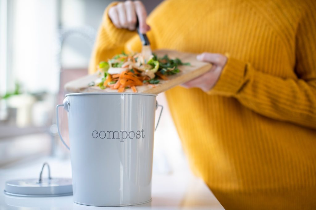 Person adding vegetable scraps to a compost container