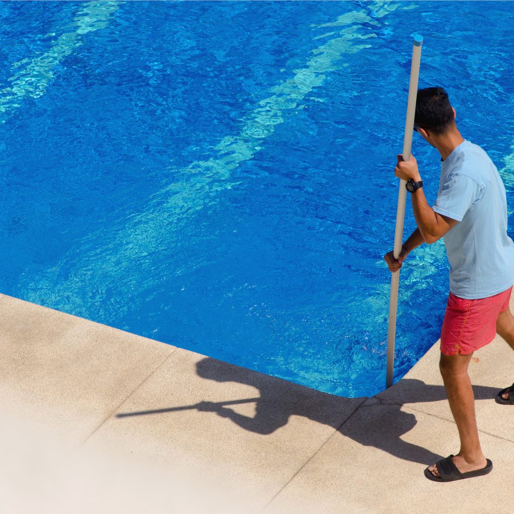 Man using skimmer to clean pool