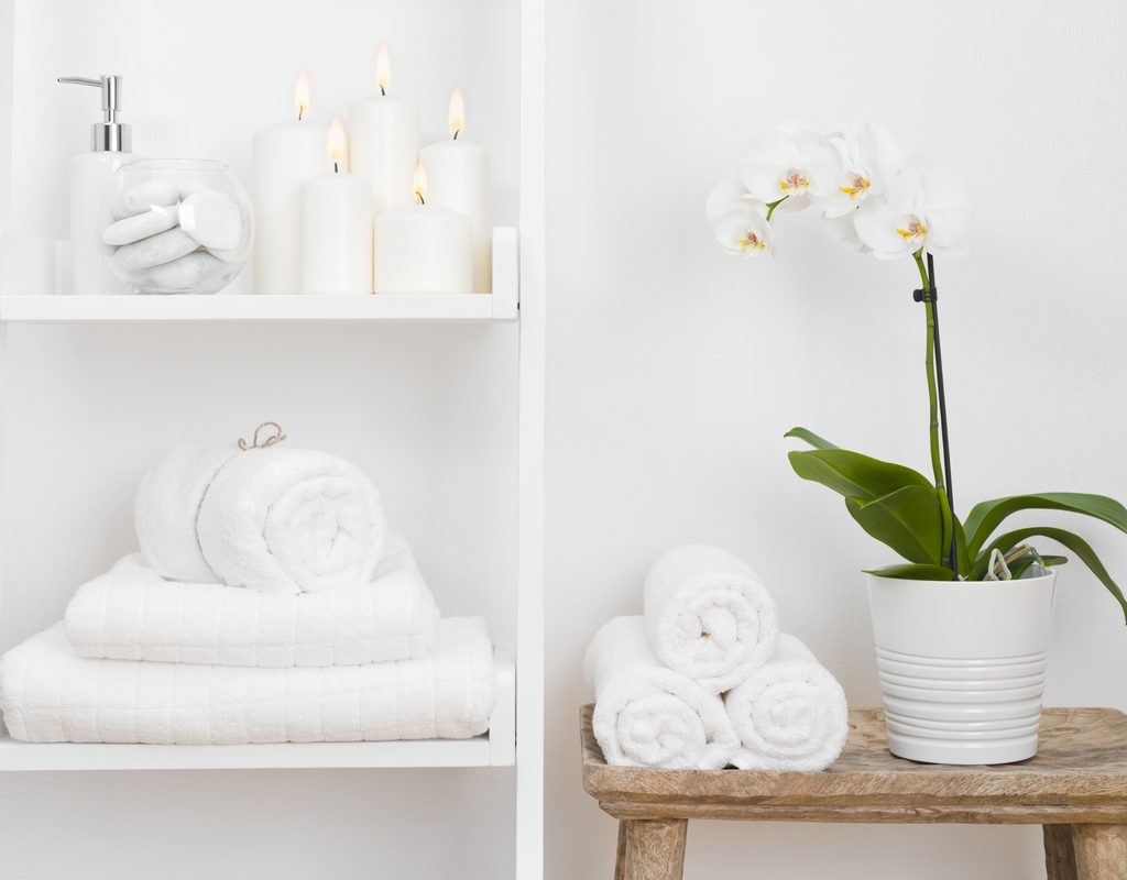 An orchid in a pot on a stool in the bathroom next to towels