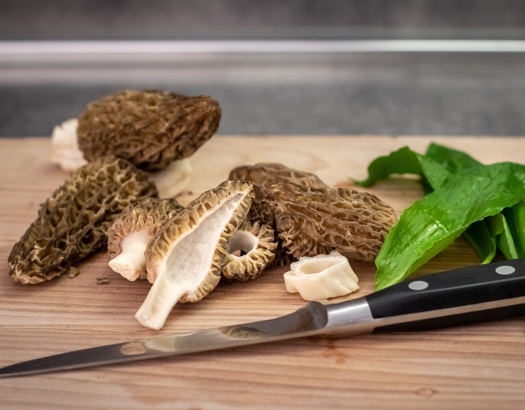 Morel mushrooms on a cutting board, one cut in half to show the hollow center
