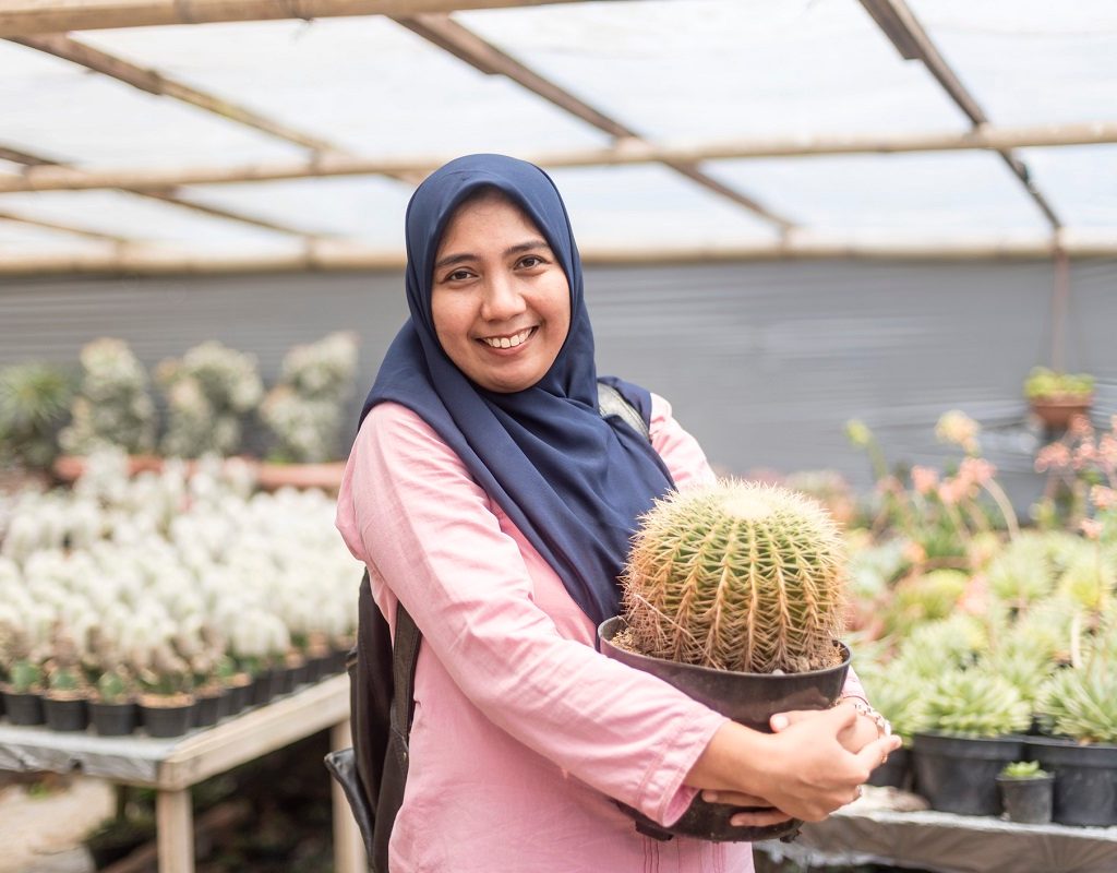 A woman smiling and holding a large round potted cactus
