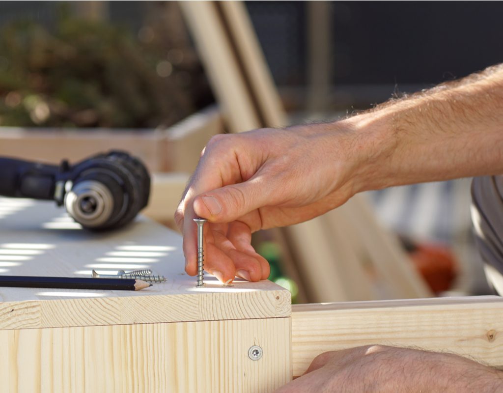 A person lining up a metal screw with a piece of wood