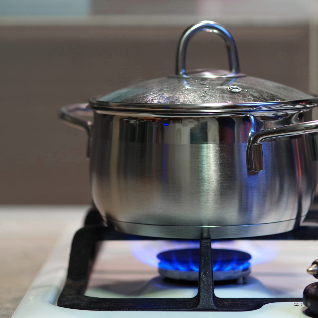 A covered, stainless steel pot on a stovetop