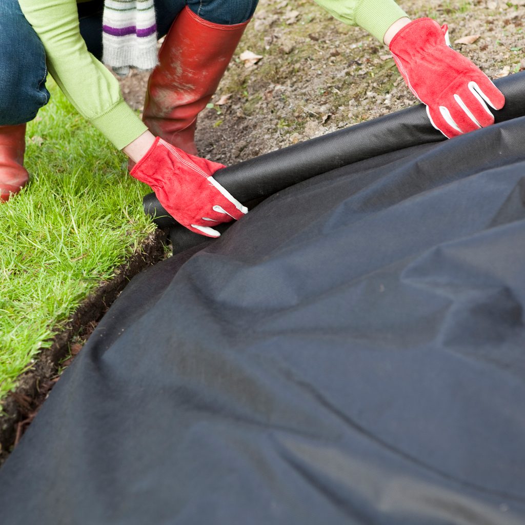 A person rolling black weed barrier cloth out over a stretch of dirt