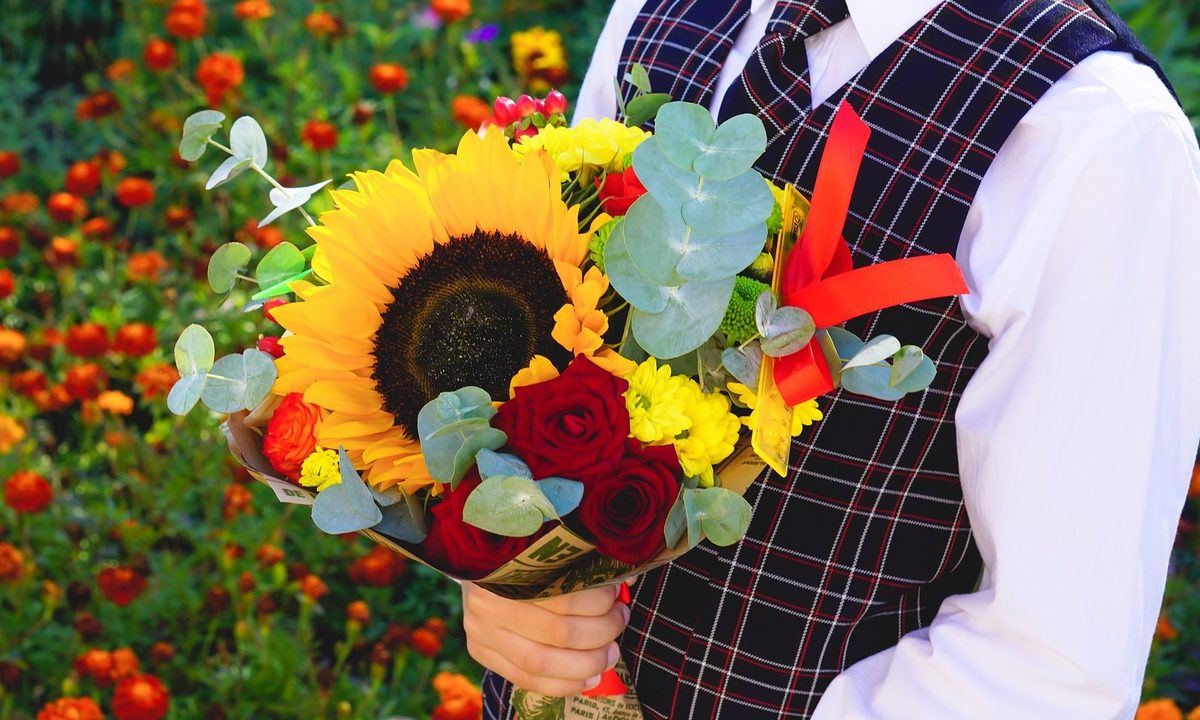 A person holding a flower bouquet with roses, daisies, eucalyptus, and sunflowers