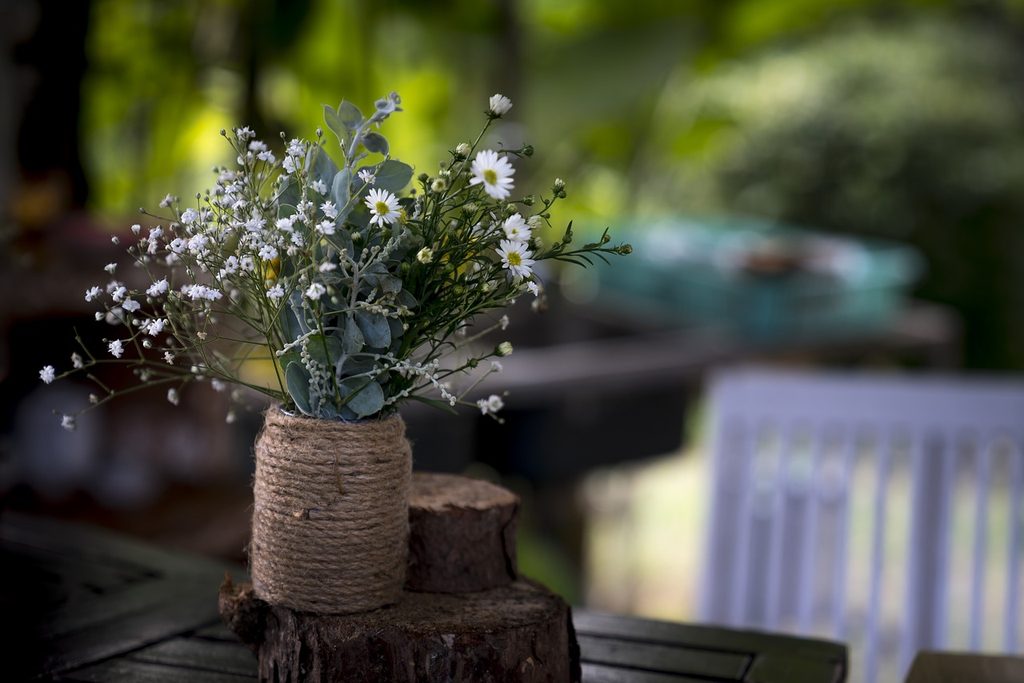 A white and green bouquet in a small vase that has been wrapped in brown string