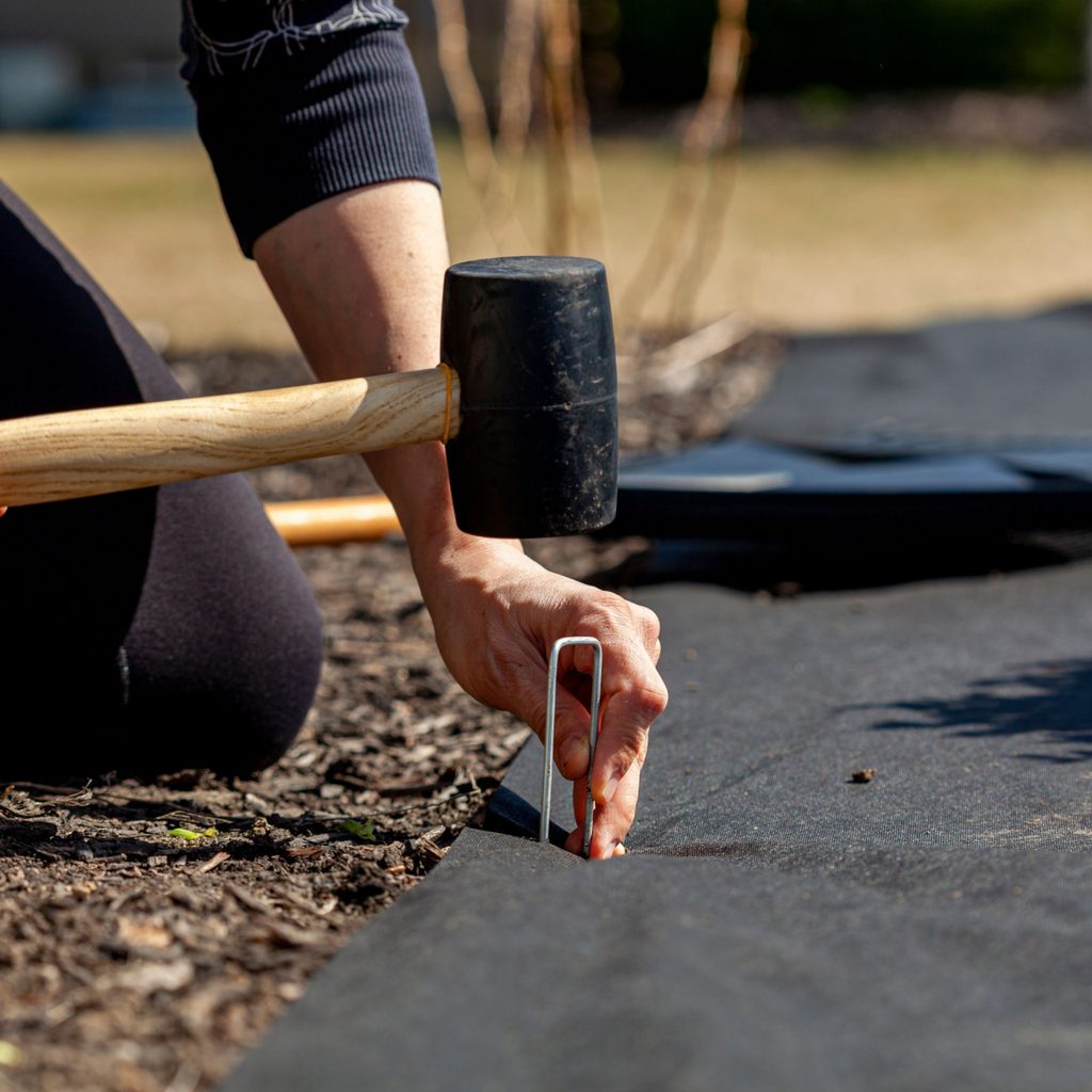 Person installing stake in landscape fabric
