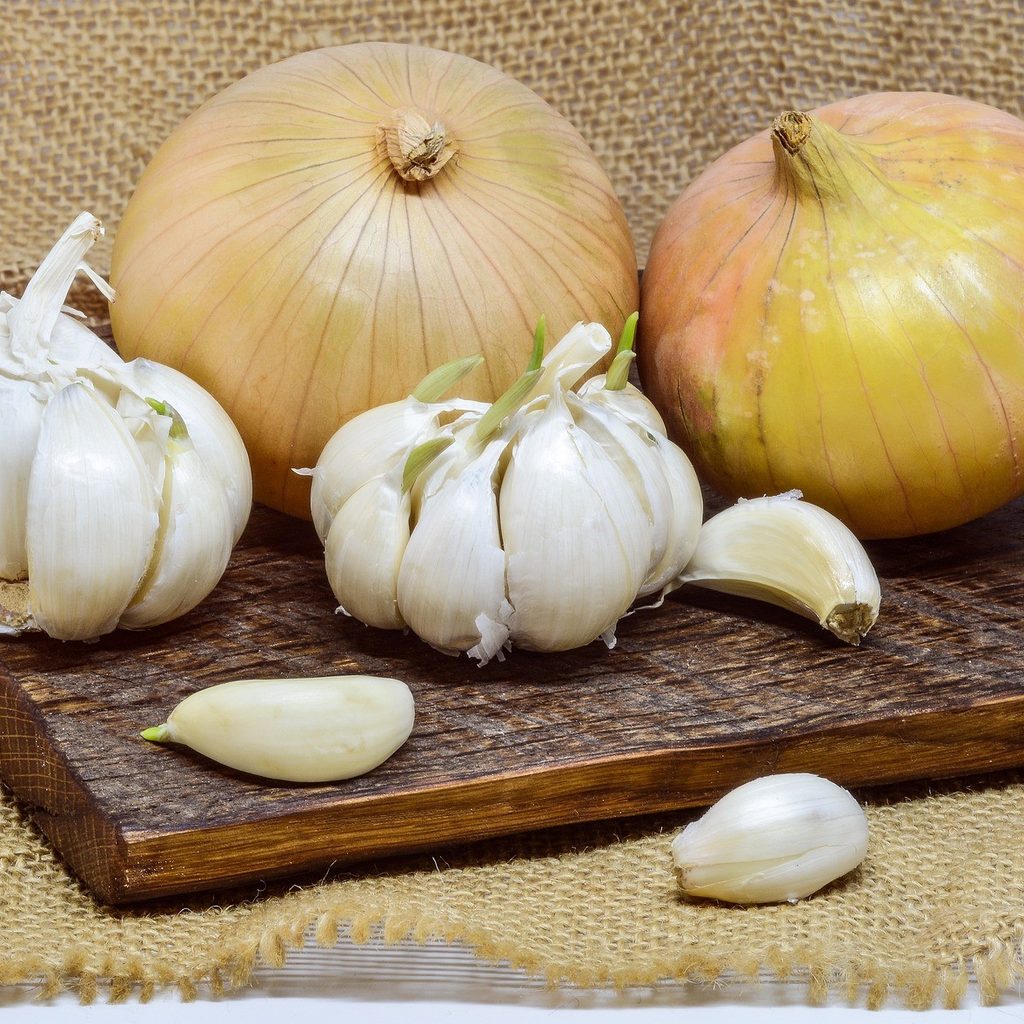 Garlic bulbs and cloves and two onions on a wooden cutting board