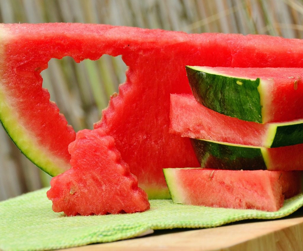 Watermelon slices in a stack. One slice has a heart-shape cut out of it, with the heart shaped watermelon piece propped in front of it.