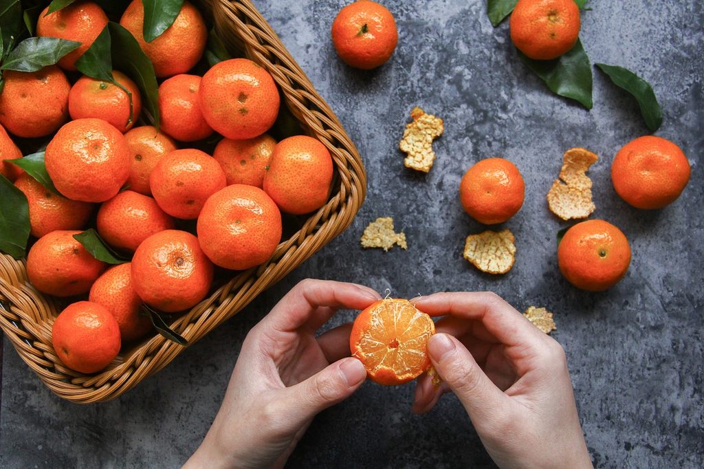 A person with a basket of oranges, peeling them.