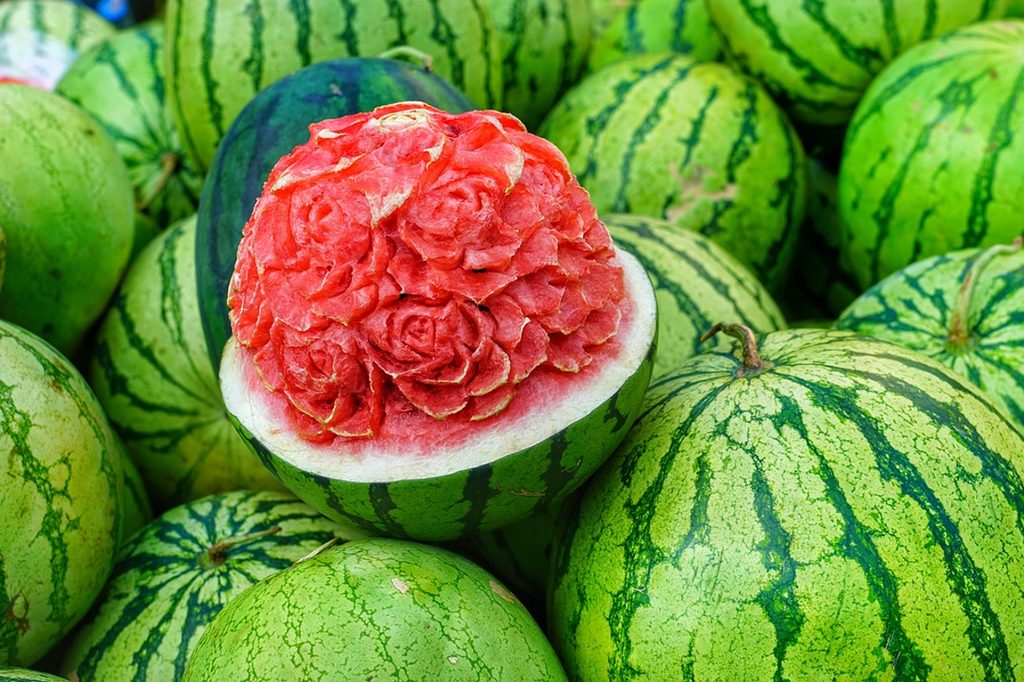A pile of watermelons with one carved into the shape of roses