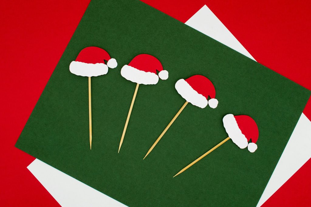 Small paper santa hats on toothpicks sitting on green, red, and white paper