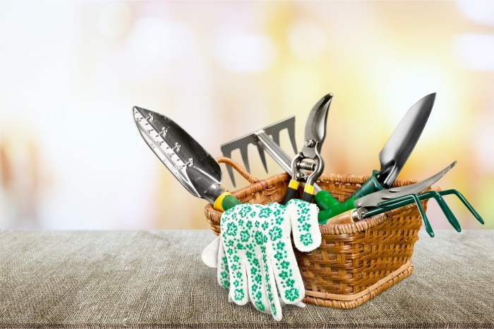 A small wicker basket on a table containing several gardening tools with green and yellow handles and floral gardening gloves