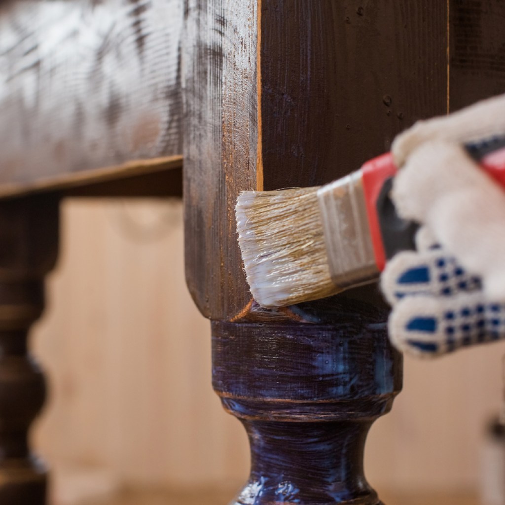 Gloved hand painting a wooden chair leg