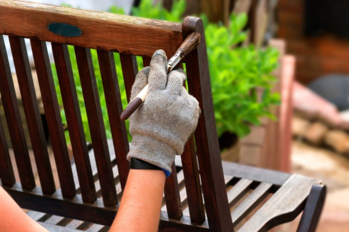 Woman wearing gloves painting the back of a garden bench