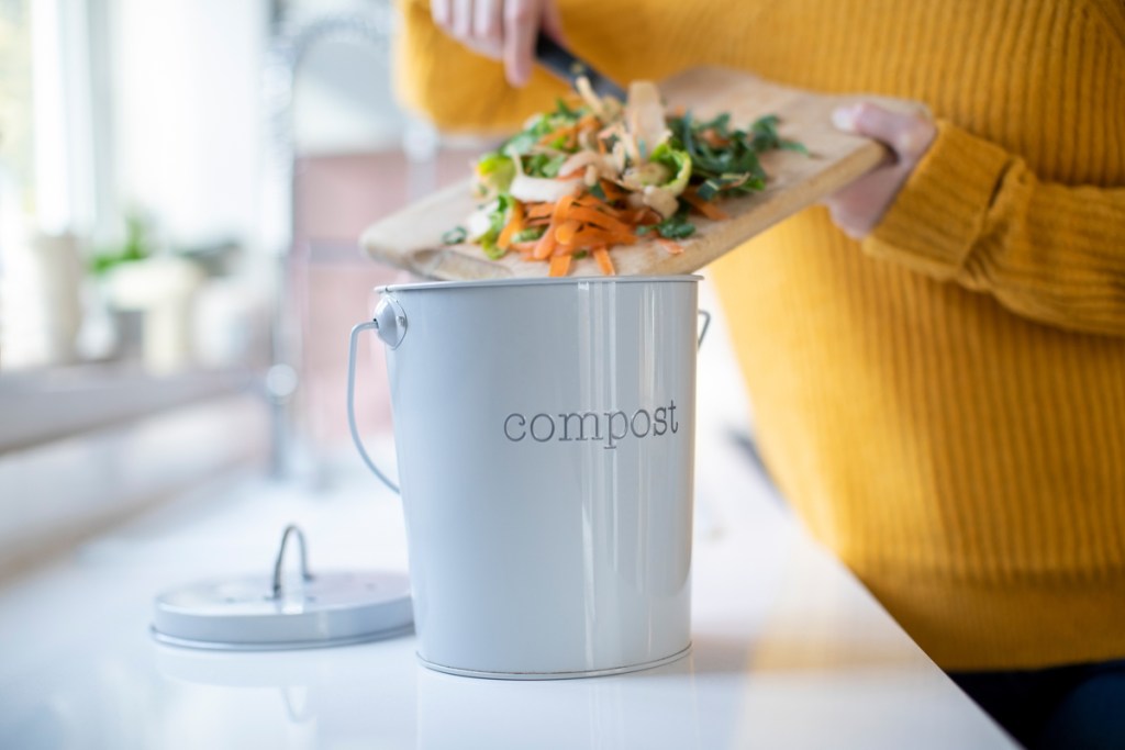 A small bucket labeled compost on a counter. A woman puts scraps into it.