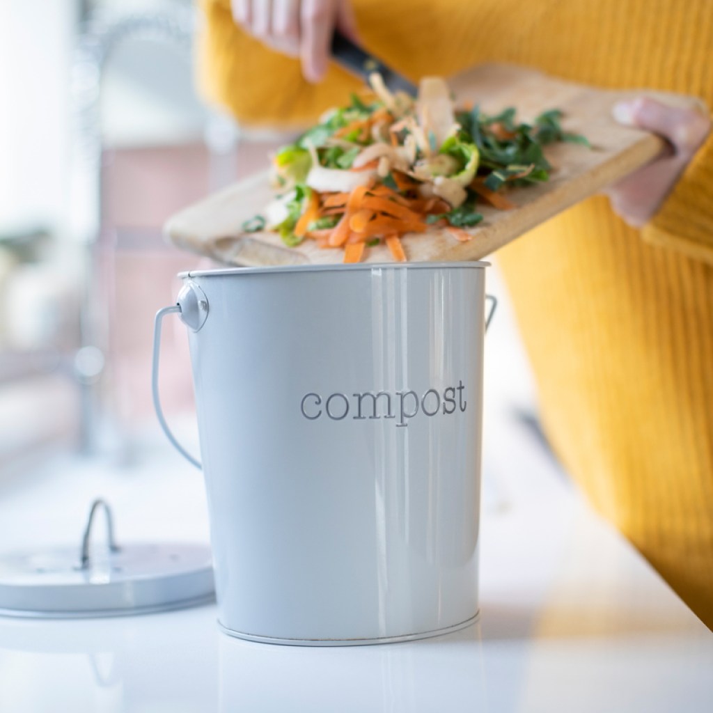 A small bucket labeled compost on a counter. A woman puts scraps into it.
