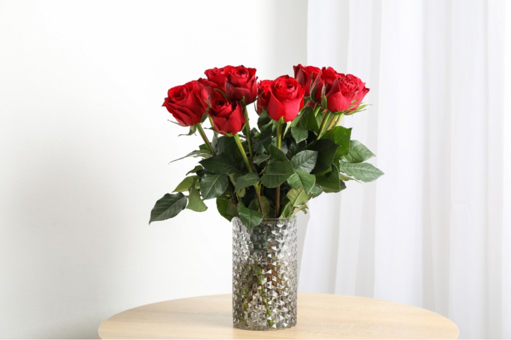 Red roses in a clear vase, on a light brown table against a white background