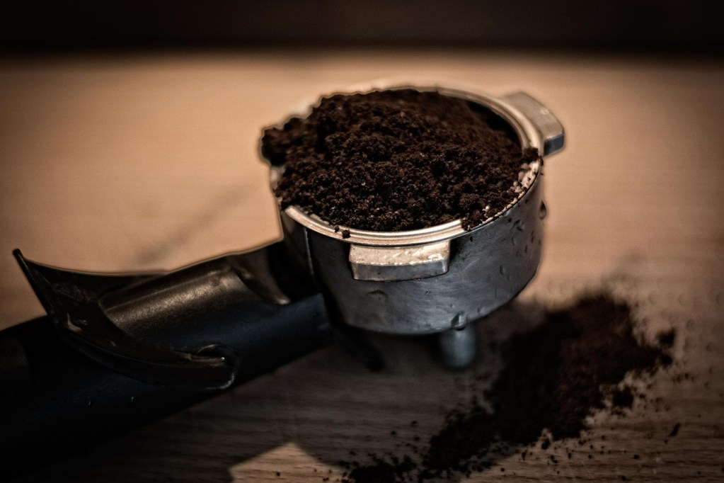 Dark coffee grounds in a silver measuring scoop