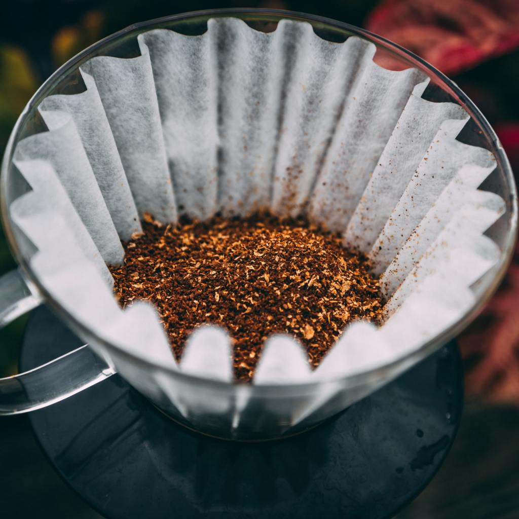 A coffee filter with coffee grounds, sitting on top of a coffee maker with plants in the background