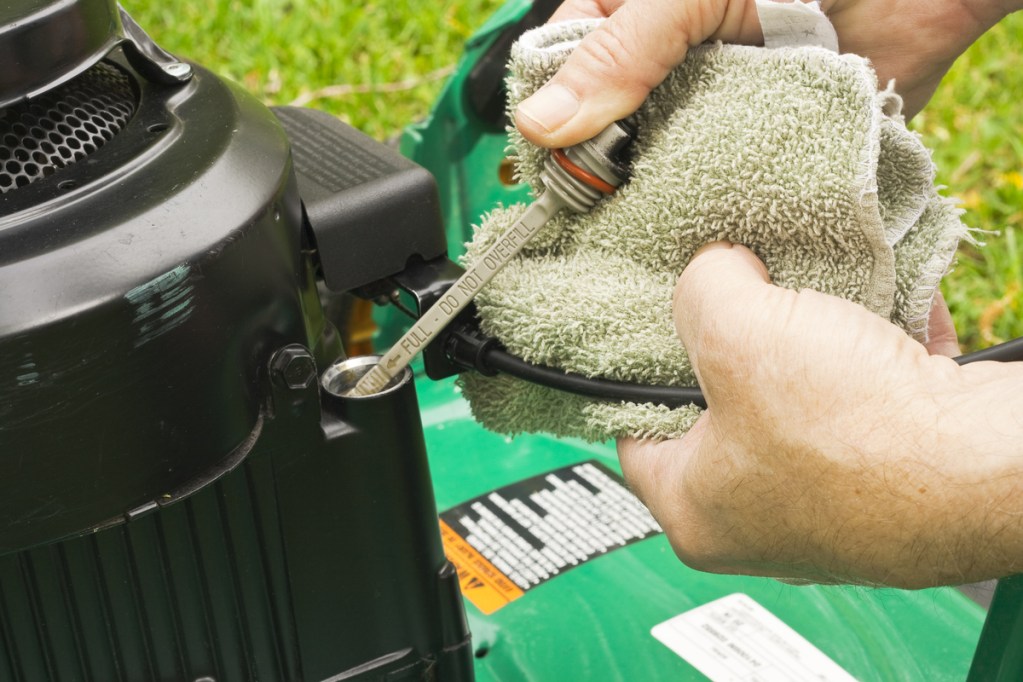 Person removing oil dipstick from lawn mower and wiping it with old, white wash rag