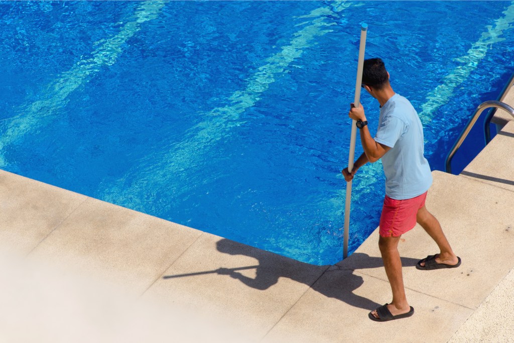 Man using skimmer to clean pool