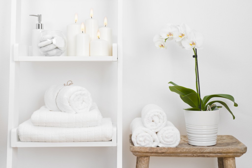 An orchid in a pot on a stool in the bathroom next to towels