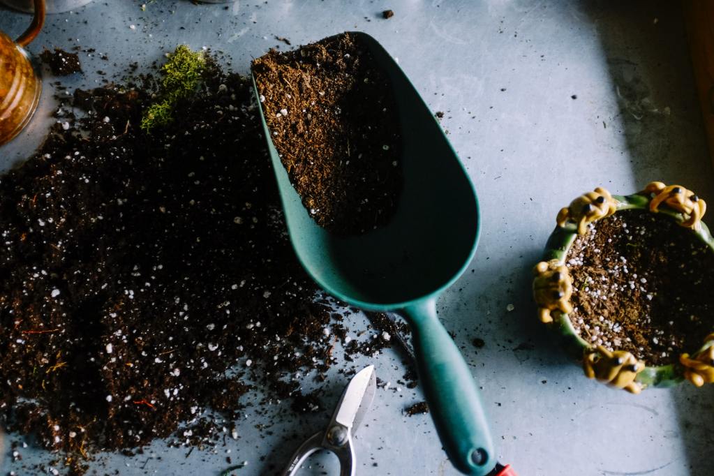 Potting soil spilled on a table with a blue metal hand shovel