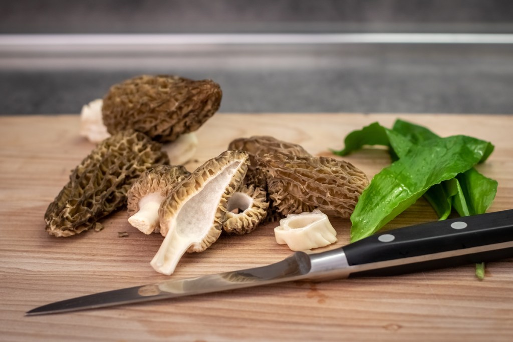 Morel mushrooms on a cutting board, one cut in half to show the hollow center