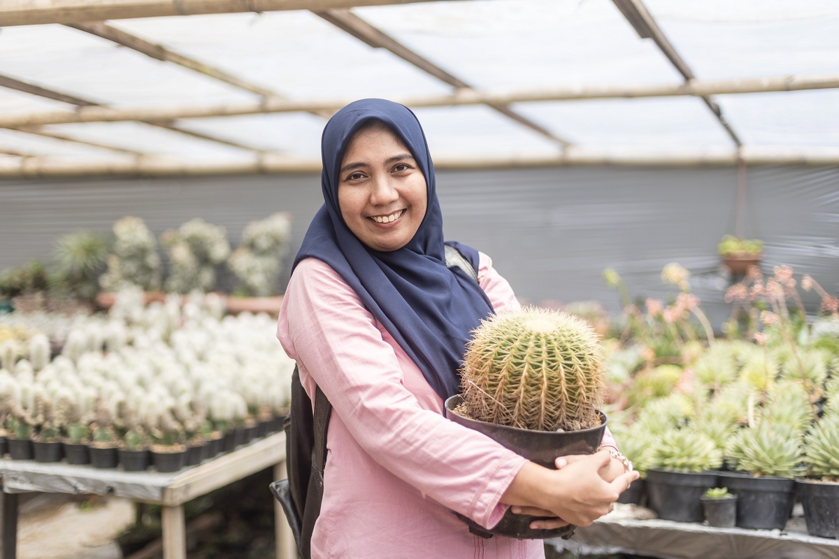 A woman smiling and holding a large round potted cactus