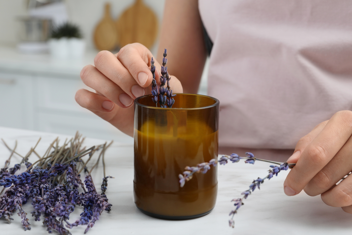 A woman adding sprigs of lavender to a homemade candle in a brown glass jar