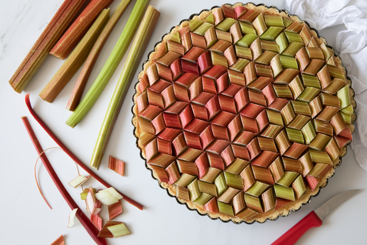 A fresh rhubarb pie with rhubarb pieces arranged geometrically on top and a few rhubarb stems sitting next to it