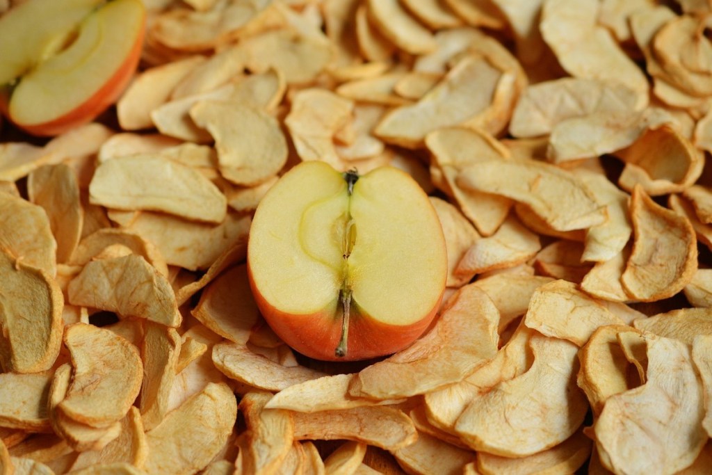 Half of an apple laying on a pile of dried apple slices