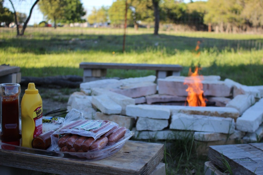 Large round fire pit with a table with hot dogs on it