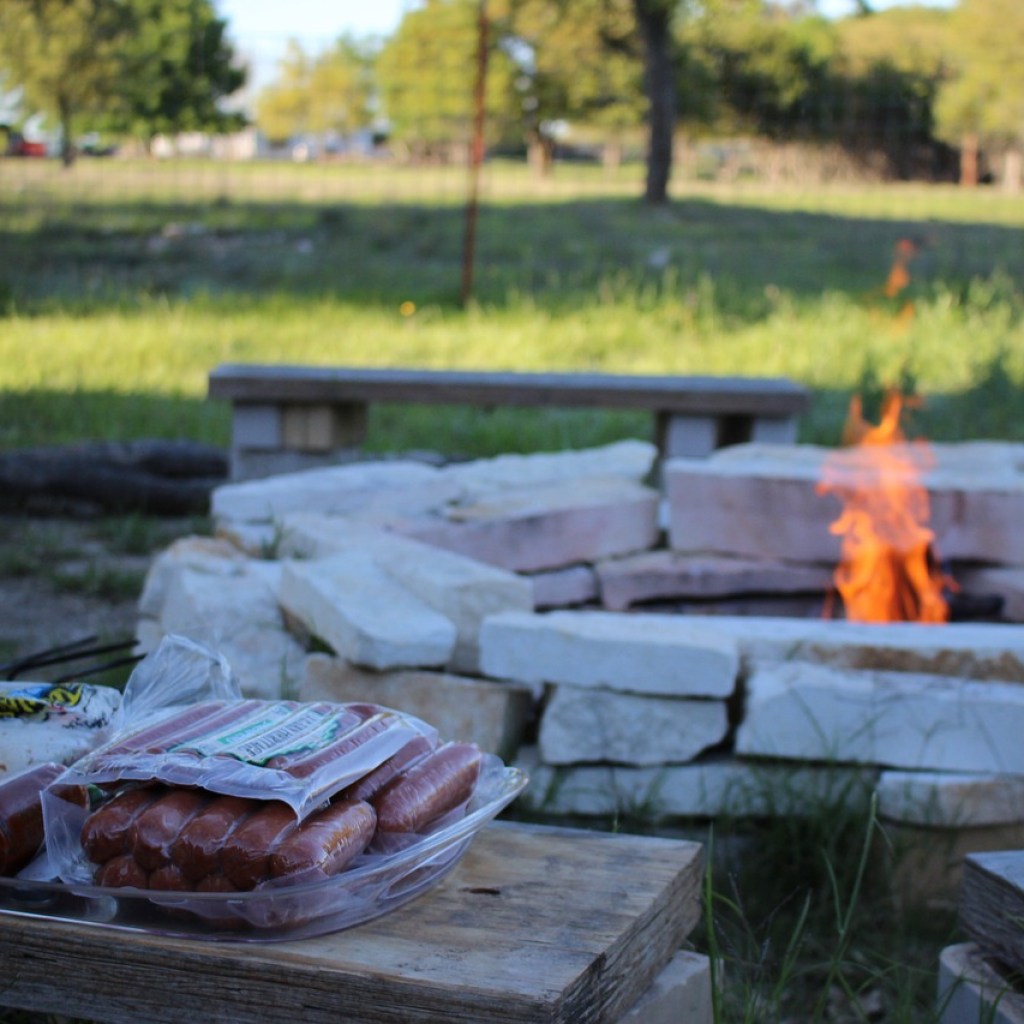 Large round fire pit with a table with hot dogs on it