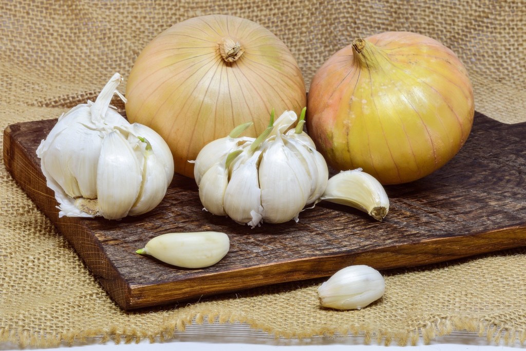 Garlic bulbs and cloves and two onions on a wooden cutting board