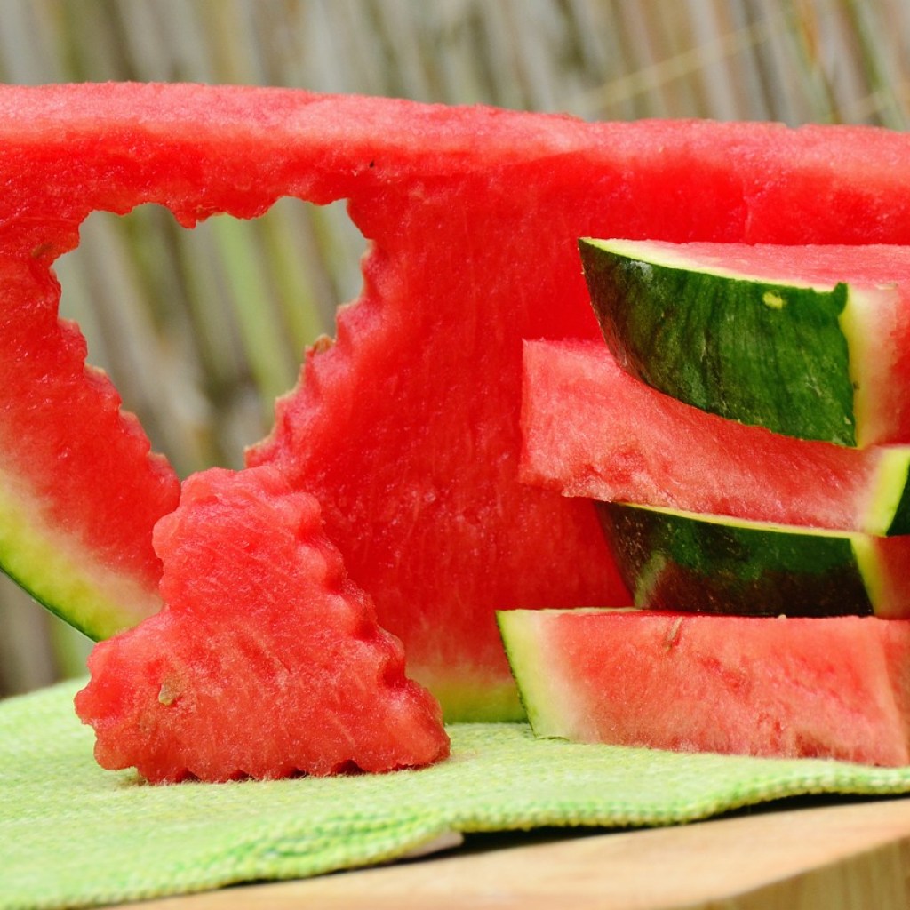 Watermelon slices in a stack. One slice has a heart-shape cut out of it, with the heart shaped watermelon piece propped in front of it.