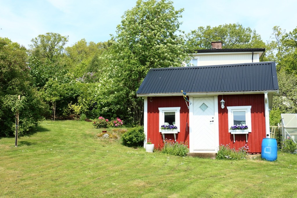 A red cottage with a blue rain barrel and a large yard.