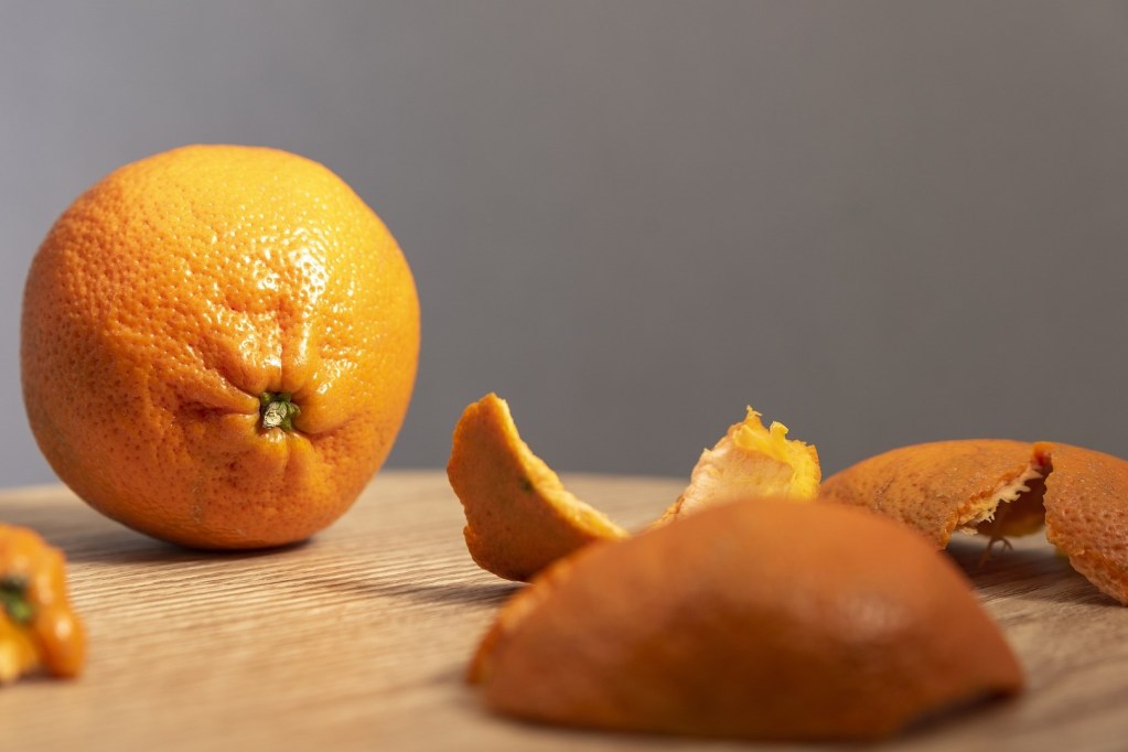 A whole orange and a pile of orange peels on a wooden table